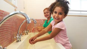 Zwei lächelnde Kinder die sich gerade bei dem Waschbecken die Hände waschen