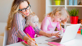 Frau mit zwei Kindern, geöffneten Laptop, Schreibblock und Kugelschreiber in der Hand.