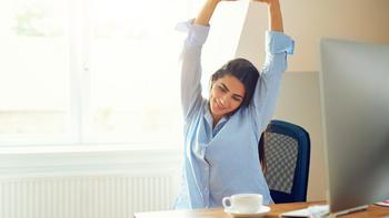 Eien Frau die zu Hause vor dem Esstisch mit einem Computer sitz und sich streckt