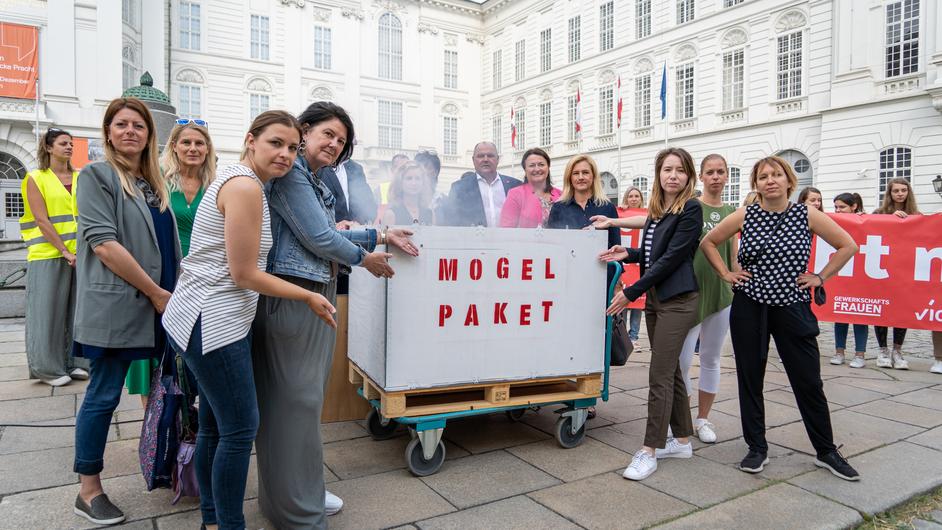 Symbolisch, eine sehr große Kiste mit der Aufschrift "Mogelpaket" und rundherum eine Menschenmenge